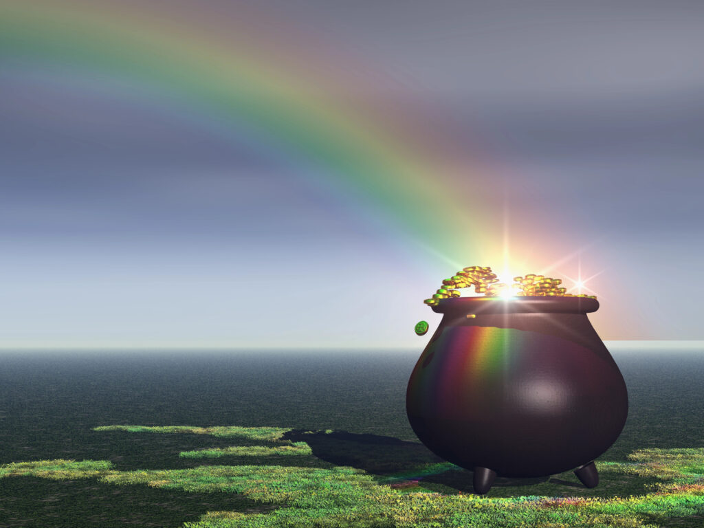 Rainbow terminating in pot of gold resting on land next to the sea.